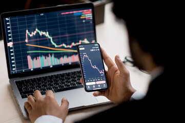 Close-up of laptop and smart phone screen with diagrams. Crypto, stock trader investor broker using smartphone and laptop for cryptocurrency financial market analysis, buying or selling cryptocurrency
