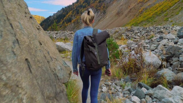 A young beautiful slender woman alone in the mountains. She walks in a denim jacket and jeans and enjoys the beautiful scenery of the highlands in autumn. Hiking. Georgia. A lonely journey.