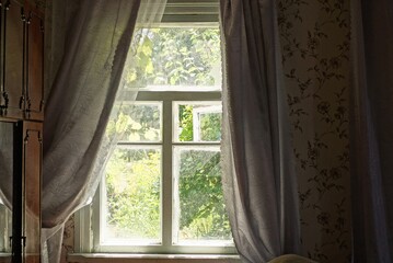 one old gray window with curtains in the room on a bright summer day