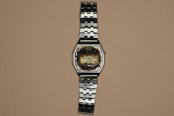old dirty broken metal gray electronic watch with an iron strap lies on a brown table