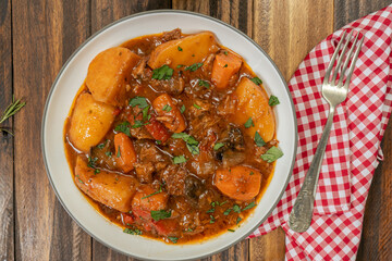Aerial view of a plate with homemade meat, potato and vegetable stew on a wooden table