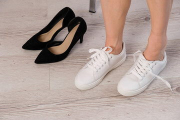 Naklejka premium Close-up business woman takes off her shoes puts on white leather sneakers.