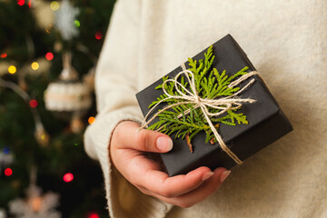 Cozy gift box in womans hands. Decorated Christmas tree on background.
