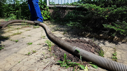 the worker opened the sewer hatch and inserted a hose for cleaning the septic tank. maintenance of communications in a private house. dirty work - obrazy, fototapety, plakaty
