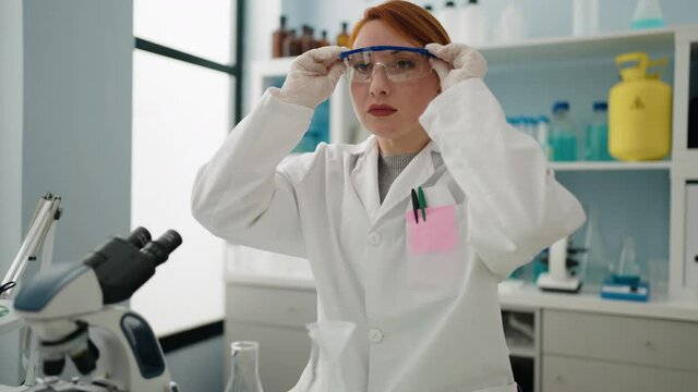 Young redhead woman wearing scientist uniform and security glasses at laboratory