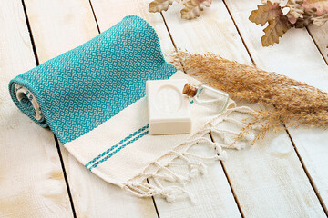 Soap and oil with turquoise and blue Turkish towel on white table. 