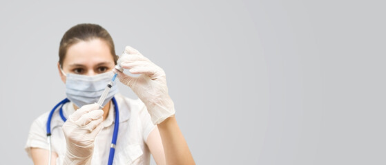Medical concept. Doctor with a syringe and ampoule in his hands on a gray background with copy space.