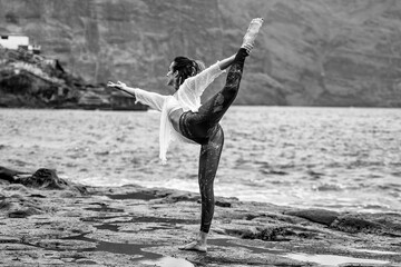 Active sporty woman standing in yoga pose on the rocks. Slim women practicing ,balancing, back bending asana. Exercise on the beach. Fit body. Morning routine. Yoga retreat.