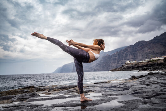 Active sporty woman standing in yoga pose on the rocks. Slim women practicing ,balancing, asana. Exercise on the beach. Fit body. Morning routine. Yoga retreat.