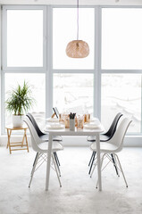 White contemporary dining room with big window. A table served for Christmas. Loft intetior in white colors. Stylish Light room with an elegant firniture Comfort home. 