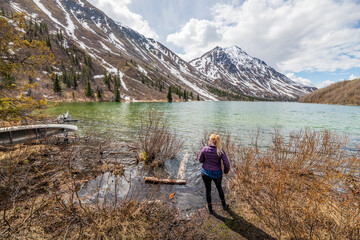 Hiker standing beside a pristine lake in northern Canada with a stunning snow capped mountain background landscape. Tourism, travel shot in Yukon Territory. 
