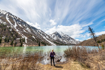 Fototapeta na wymiar Tourism, travel shot of woman hiker standing beside a northern, isolated lake during spring time with stunning mountains, pristine lake in the background. 