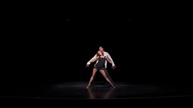 Latin-american ballroom dance.Performance fragment.2 dancers on dark stage twisting,making feet and hand swings,lunges,passionate tango movements,heart shape forming with their bodies.Studio concept