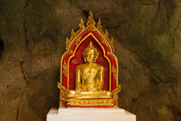 One of the many sculptures of the Buddha against the background of a stone wall. Cave temple of Wat...