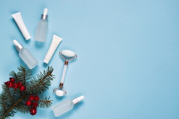 Set of cosmetic products. Skin care cream,roller massager, moisturizing lotion, fir tree branches on a blue background. Facial beauty cosmetic spa product. Natural Winter cosmetic products. Top view