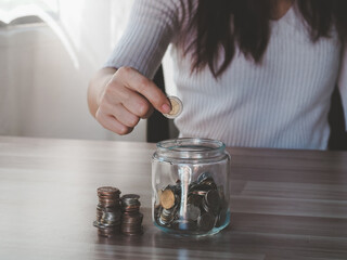 Woman handling drop a coin in glass jar with money coin stack growing for business. financial and accounting concept. bank account balance payment.