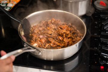 Hand using kitchen flipper frying sliced beef in iron pan on stove