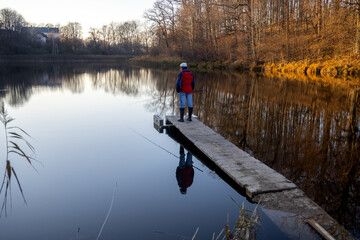Fototapeta na wymiar Lonely woman fishing with a rod in little village lake or pond. Spare time in nature on a beautiful autumn sunny evening