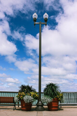 Street light post with two big flower pots on each side. On the left a brown bench. The post is in front of the water on navy pier.