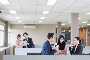 Asian officer talking with their coworker in the office while having a coffee break.