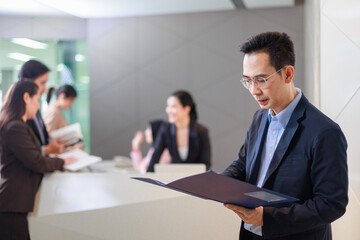 Portrait of confident Asian businessman using digital tablet while colleague in background.
