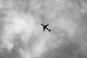 Black and white image of a single plane flying across a cloudy sky
