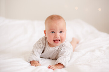 the baby is lying at home on the bed smiling