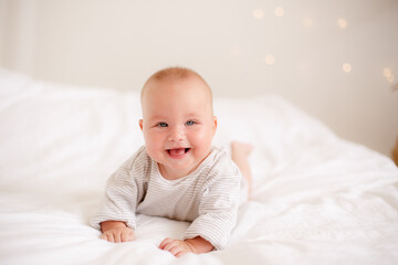 the baby is lying at home on the bed smiling
