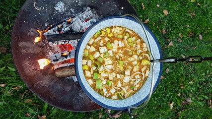 Large pot over a fire bowl, cooking vegetable soup in cast iron cauldron outdoors. Aerial view.