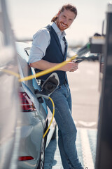 Young busnessman waiting for his electric car to charge