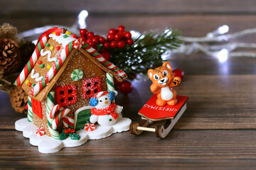 A toy house with a snowman, a tiger - the symbol of 2022 on a wooden surface, blurred lights in the background
