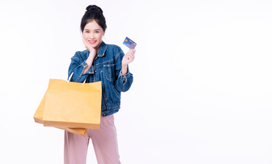 Excited cheerful smile shopper asian woman wear jacket jeans holding shopping bags paper showing credit card mockup while standing over isolated white background. Payment finance electronic concept. 