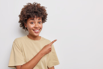 You should check it out. Beautiful woman smiles happily points index finger at upper right corner shows best choice promots product dressed in casual beige t shirt isolated over white background