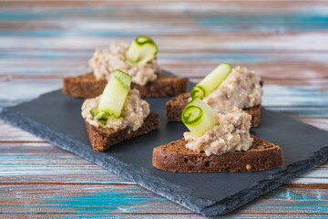 Appetizer, herring, onion and boiled egg forshmak on fried rye bread on a slate or stone board on a wooden background. Jewish cuisine.