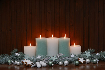 Weihnachtshintergrund: Brennende Kerzen mit Weihnachtsdeko vor einer Holzwand.