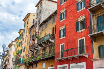 Naklejka premium Colored facades of old buildings with balconies decorated with plants in the old part of Verona. Traditional Italian buildings