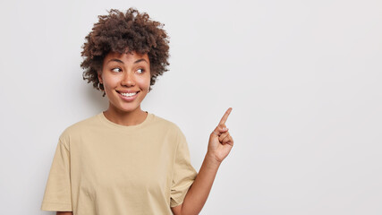 Horizontal shot of pretty good looking woman with curly hair points index finer above at promo...