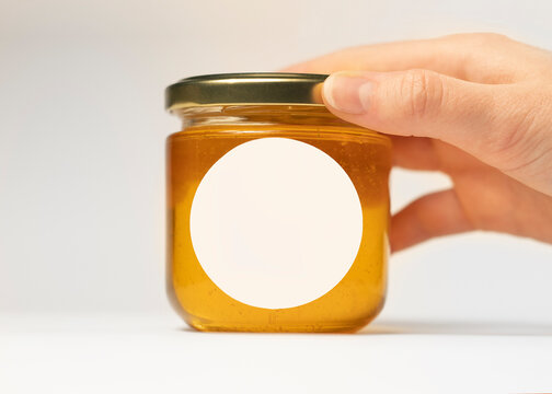 A woman's hand puts a jar of honey on the table with a round sticker with plotter cutting. with space for packaging design