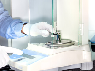 A operator's hand is holding steel calibration weight to place on the analytical balance. Concept...