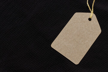 Price tag or blank cardboard label with thread isolated on the black cloth. Great for clothing or...