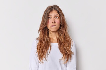 Fototapeta premium Thoughtful European woman with long hait bites lips considers something has pensive expression dressed in casual jumper isolated over white background makes plan in mind searches for solution
