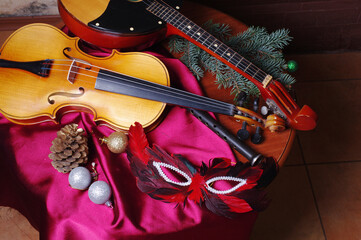 Fototapeta premium Violin, pipe, domra, carnival mask and Christmas tree branch on a table with a burgundy tablecloth 
