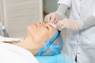 Photo of professional female cosmetologist using sponges to wash the face of a woman client preparing for a cosmetic procedure. Rejuvenating and moisturizing procedures