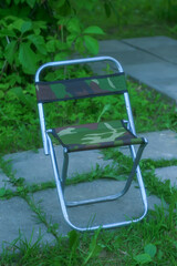 Small folding tourist chair. Close-up. Blurred green background. Top view.