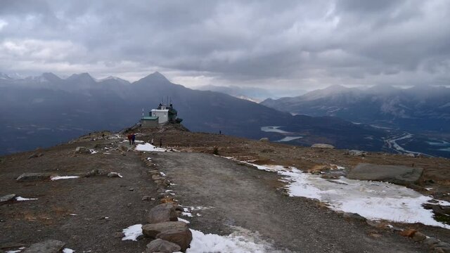 Tourists hiking in front of the mountain station of a cableway near Jasper, Alberta, Canada in the Rocky Mountains on snowy day in autumn season with cloudy sky.