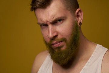 a bearded man with a serious expression in a white t-shirt with tattoos on his arms