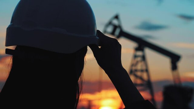 Industrial, oil and gas concept. Silhouette working engineer oil rig. Oil rigs at sunset. Silhouette of woman engineer with tablet overseeing the site of crude oil production at sunset.