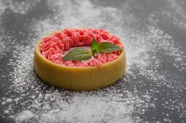 Cake with cream and mint leaf on a black surface, sprinkled with powdered sugar.