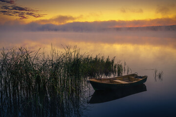 Fototapeta na wymiar Boat on the lake in the rays of the rising sun and fog, zemborzycki lake