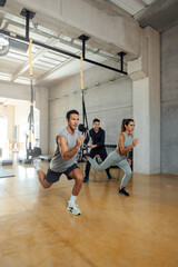 Suspension workout. Coach trains man and woman to do lunge exercise in a gym.